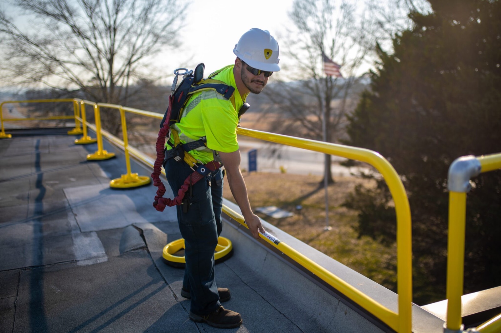 Worker on a rooftop resting a hand on a non-penetrating yellow guardrail standing on round counterweighted bases