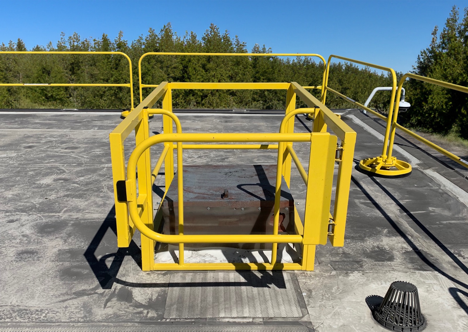 Yellow guardrail and self-closing gate ringing a roof hatch opening, with non-penetrating mobile rail behind it