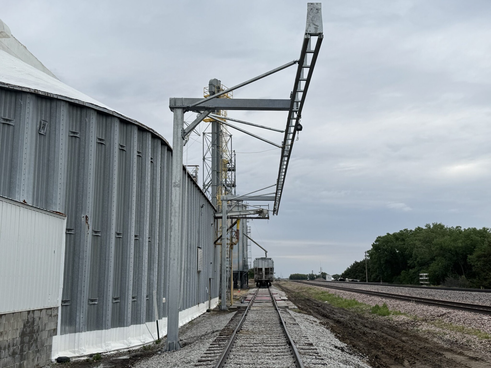 Cantilevered free-standing overhead fall-arrest rail reaching out over a railcar loading spur at a bulk terminal