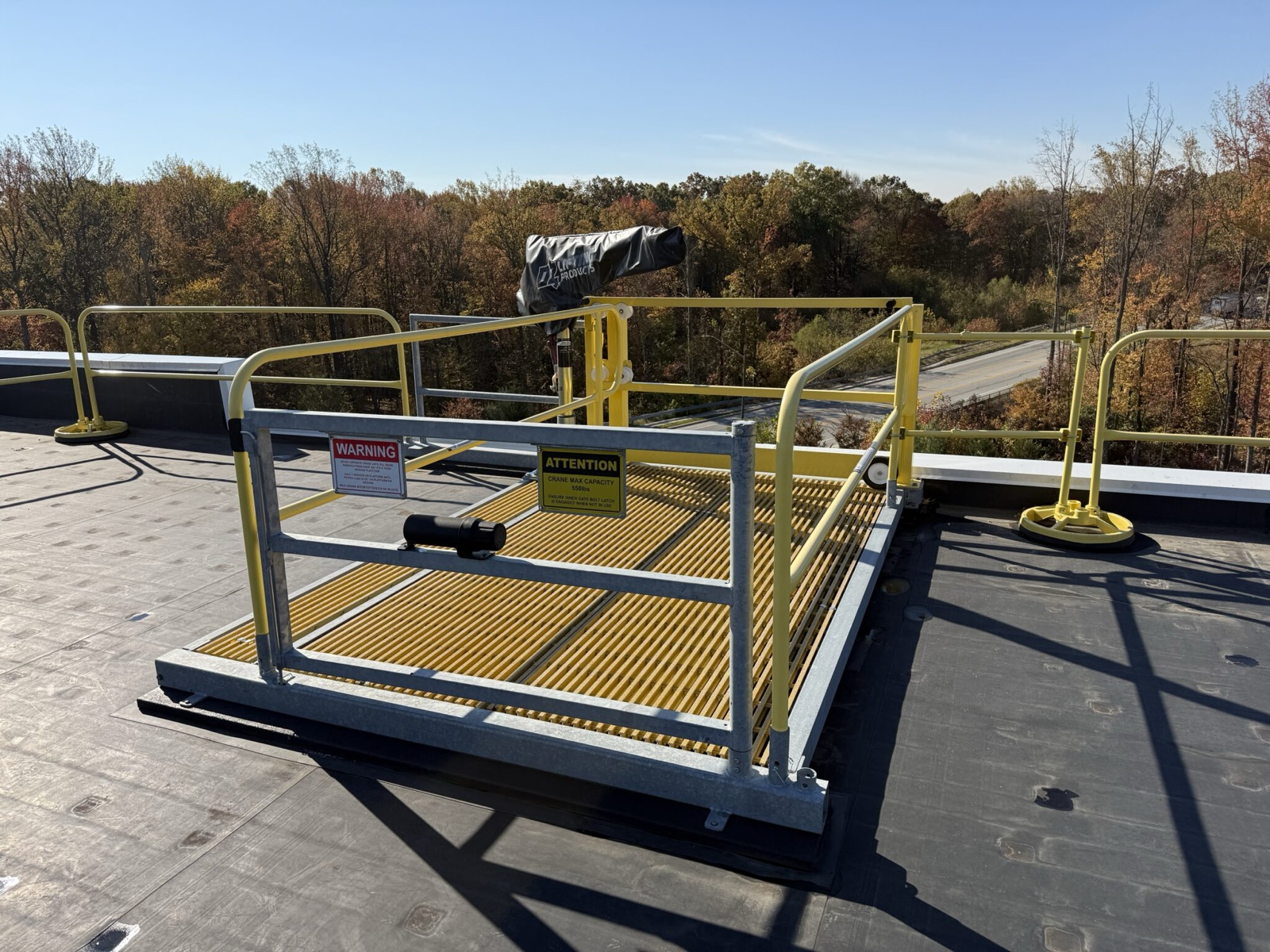 A modular rooftop work platform with yellow grating, guardrail, and a self-closing gate