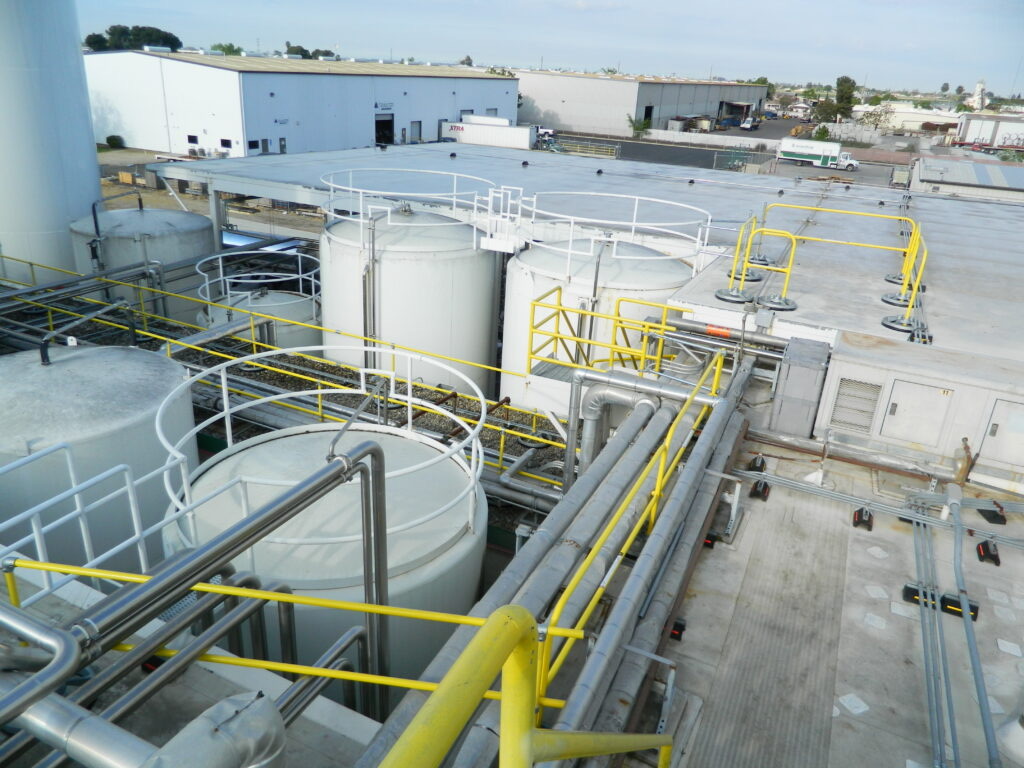 Rooftop dairy-processing install with yellow guardrail and modular crossover platforms among process tanks